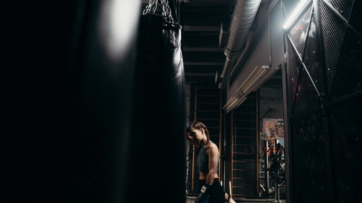 A strong female boxer intensely trains with a punching bag in an industrial-style gym.